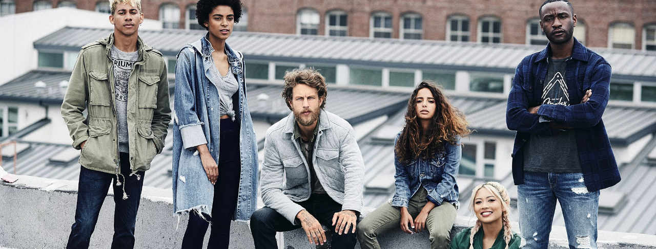 6 young people sitting on a rooftop dressed in lucky brand jeans.
