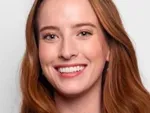 Portrait photo of a person with auburn hair smiling against a light background.