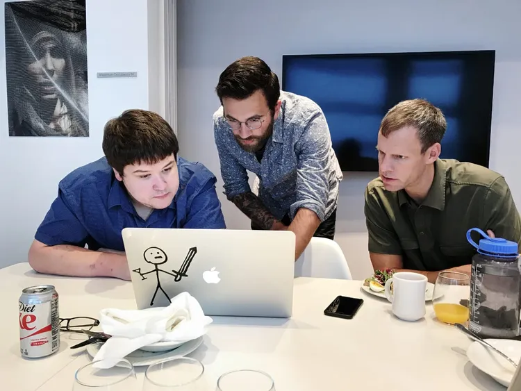 3 guys staring at a macbook.
