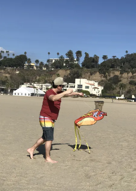 man trying to fly a kite that looks like a hot dog on a beach.