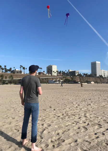man on a beach staring at 2 kites in the air.