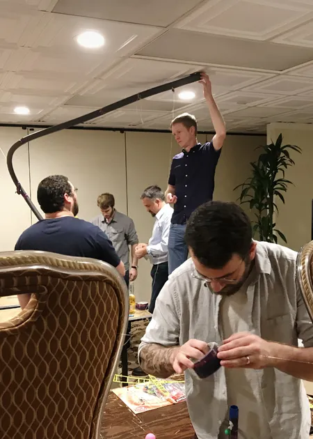 guy holding up some sort of contraption with other people working around him in a hotel room.