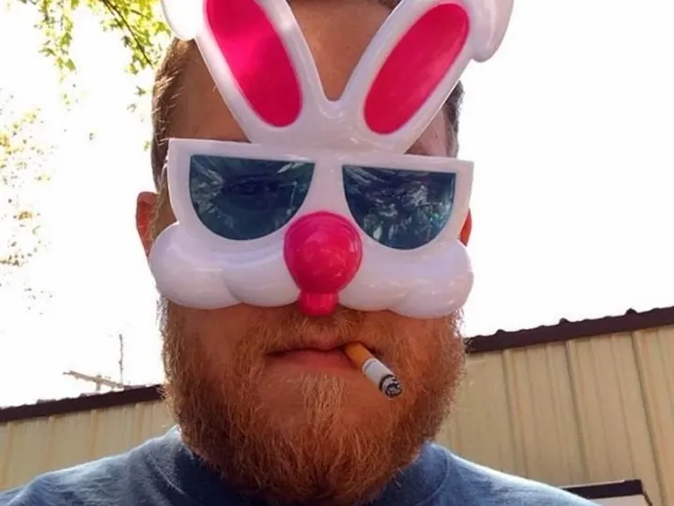 Bearded man with a funny bunny mask and a cigarette in his mouth.